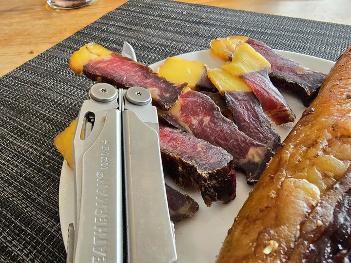 Biltongskywe met geelvet en ’n knipmes op ’n bord.