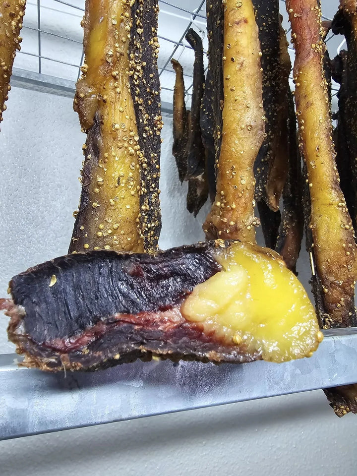 Geelvetbiltong van naby met hangende biltong agter dit.