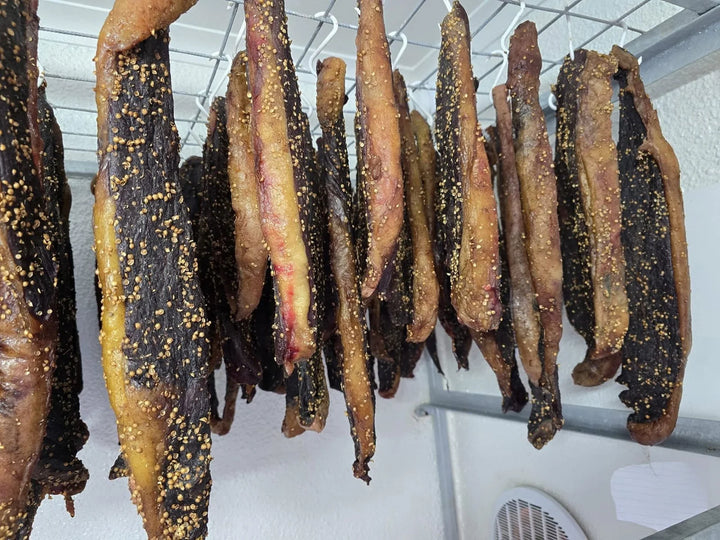 Dik stukke geelvetbiltong aan ’n rak.