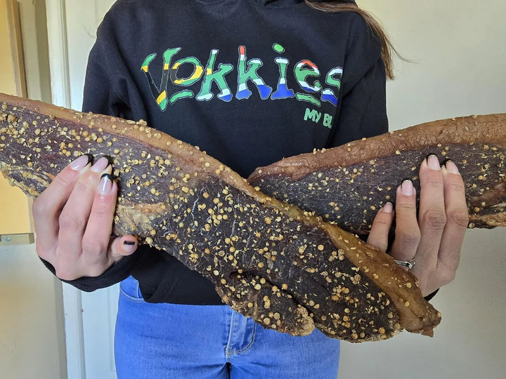 Iemand in ’n Vokkies-hemp hou twee groot stukke biltong vas.