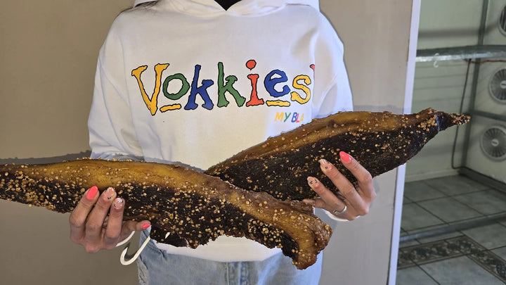Iemand in ’n wit Vokkies-hemp wys twee groot stukke biltong.